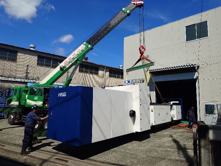 クレーンで吊り上げられ工場へ搬入されるHSG製パイプ用レーザー加工機の本体