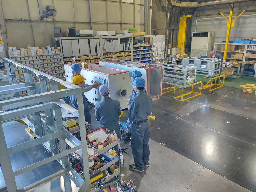 製作中の空調機器を前に説明を聞く若手社員たち